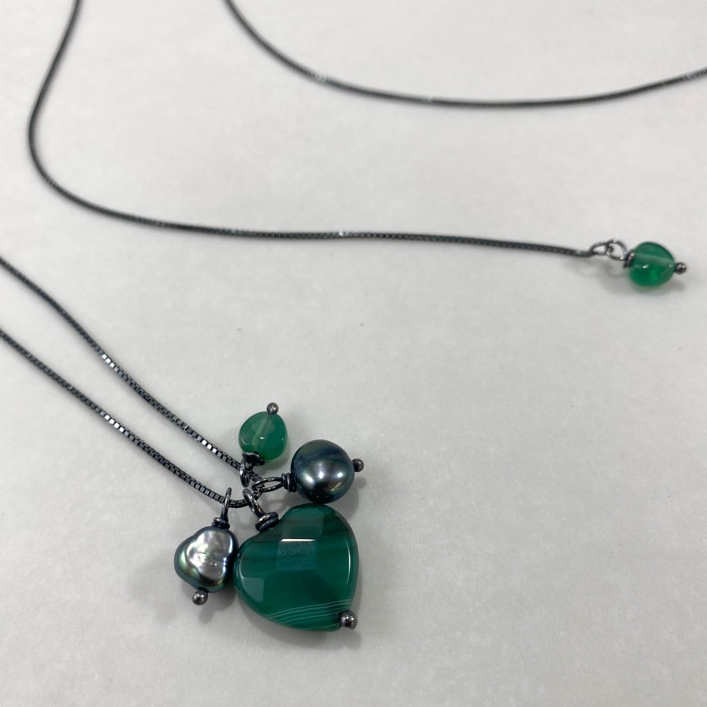 Colar corrente veneziana prata 925 oxidada (escura), com pingentes em pedras ágata verde e pérola negra. Comprimento: 70cm. Embalagem em envelope de tecido, com cartão postal Amor Maior. Esta é uma joia de prata 925 produzida com uma liga conhecida internacionalmente com STERLING SILVER – 925, o que significa que ela é constituída de 92,5% de prata pura, garantindo a qualidade do material utilizado. Por se tratar de pedras naturais, podem apresentar variações na coloração.