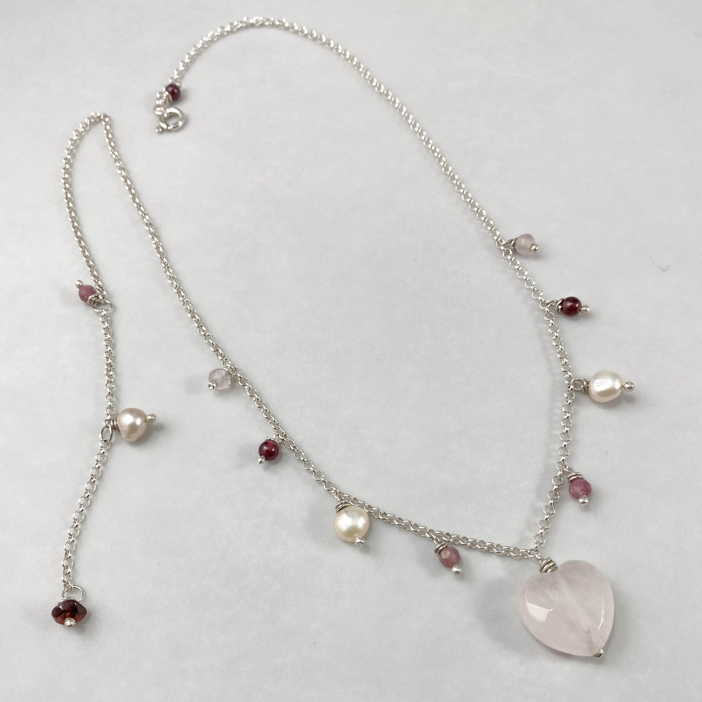 Colar corrente elo português aberto prata 925 polida (clara), com pingentes em pedras coração quartzo rosa, turmalina, pérola rosa e granada. Comprimento: 45cm. Embalagem em envelope de tecido, com cartão postal Amor Maior. Esta é uma joia de prata 925 produzida com uma liga conhecida internacionalmente com STERLING SILVER – 925, o que significa que ela é constituída de 92,5% de prata pura, garantindo a qualidade do material utilizado. Por se tratar de pedras naturais, podem apresentar variações na coloraçã