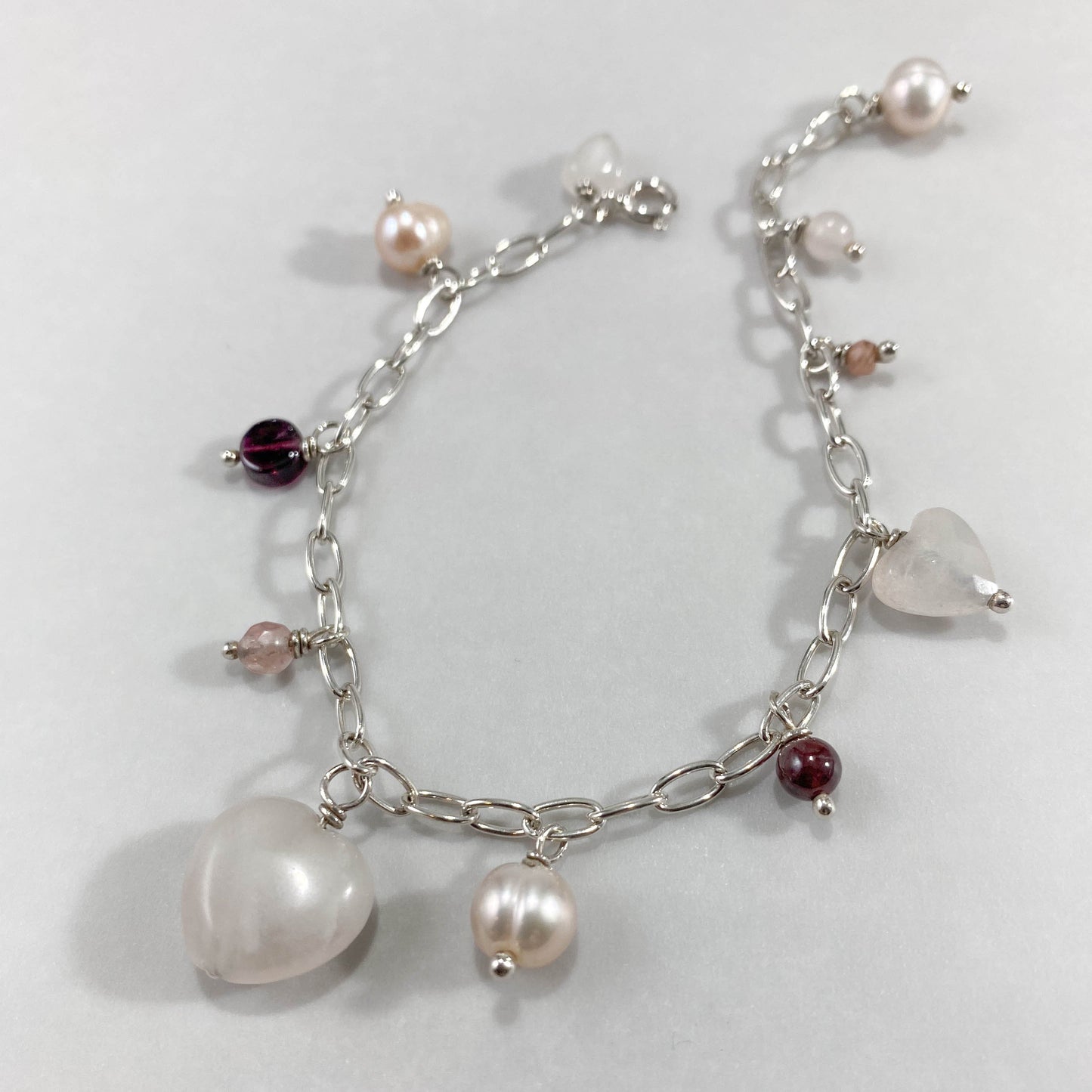 Pulseira corrente elos ovais prata 925 polida (clara), com pingentes em pedras quartzo rosa, pérola lilás, granada, quartzo cereja e rodocrosita. Comprimento: regulagem entre 15cm e 18cm. Para outras medidas entre em contato. Embalagem em envelope de tecido, com cartão postal Amor Maior. Esta é uma joia de prata 925 produzida com uma liga conhecida internacionalmente com STERLING SILVER – 925, o que significa que ela é constituída de 92,5% de prata pura, garantindo a qualidade do material utilizado. Por se