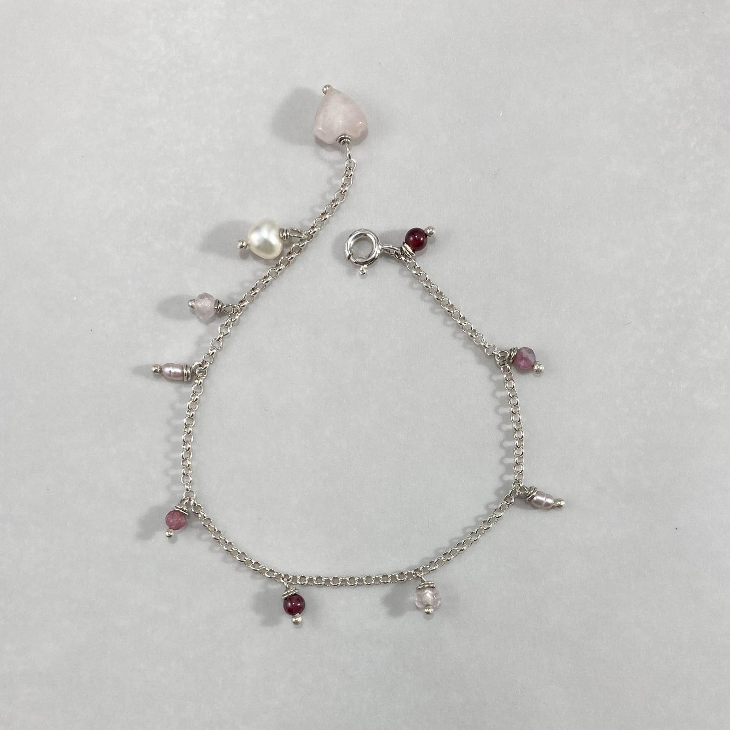 Pulseira corrente elo português aberto em prata 925 polida (clara), com pingentes em pedras quartzo rosa, pérola lilás, granada, quartzo cereja e rodocrosita. Comprimento: regulagem entre 15cm e 18cm. Para outras medidas entre em contato. Embalagem em envelope de tecido, com cartão postal Amor Maior. Esta é uma joia de prata 925 produzida com uma liga conhecida internacionalmente com STERLING SILVER – 925, o que significa que ela é constituída de 92,5% de prata pura, garantindo a qualidade do material utili