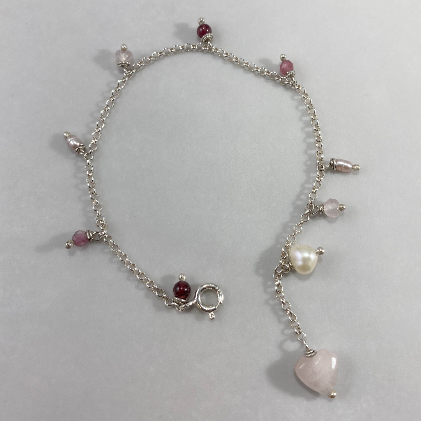 Pulseira corrente elo português aberto em prata 925 polida (clara), com pingentes em pedras quartzo rosa, pérola lilás, granada, quartzo cereja e rodocrosita. Comprimento: regulagem entre 15cm e 18cm. Para outras medidas entre em contato. Embalagem em envelope de tecido, com cartão postal Amor Maior. Esta é uma joia de prata 925 produzida com uma liga conhecida internacionalmente com STERLING SILVER – 925, o que significa que ela é constituída de 92,5% de prata pura, garantindo a qualidade do material utili