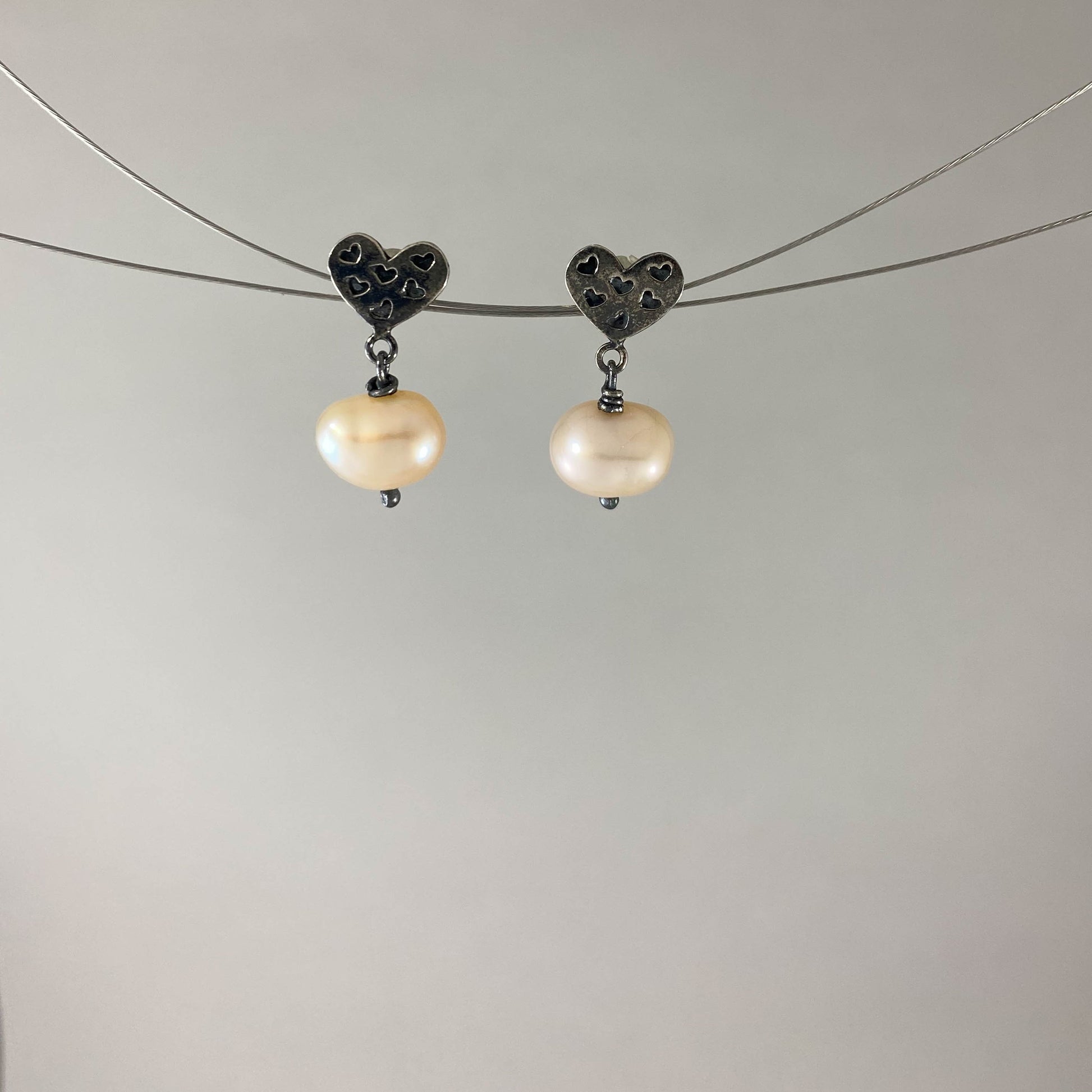Brinco base em forma de coração com mini corações em prata 925 oxidada (escura) com pérola natural. Embalagem em envelope de tecido, com cartão postal Amor Maior. Esta é uma joia de prata 925 produzida com uma liga conhecida internacionalmente com STERLING SILVER – 925, o que significa que ela é constituída de 92,5% de prata pura, garantindo a qualidade do material utilizado. Por se tratar de pedras naturais, podem apresentar variações na coloração.