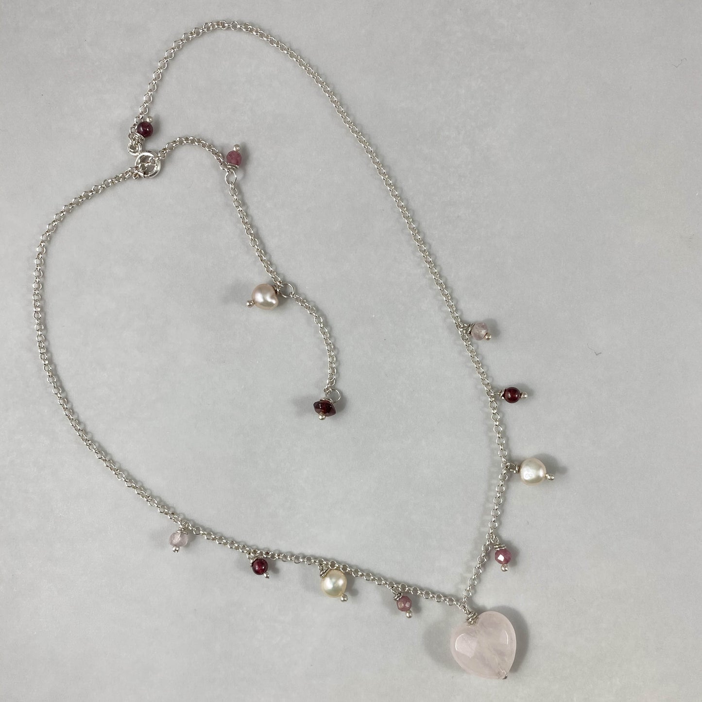 Colar corrente elo português aberto prata 925 polida (clara), com pingentes em pedras coração quartzo rosa, turmalina, pérola rosa e granada. Comprimento: 45cm. Embalagem em envelope de tecido, com cartão postal Amor Maior. Esta é uma joia de prata 925 produzida com uma liga conhecida internacionalmente com STERLING SILVER – 925, o que significa que ela é constituída de 92,5% de prata pura, garantindo a qualidade do material utilizado. Por se tratar de pedras naturais, podem apresentar variações na coloraçã