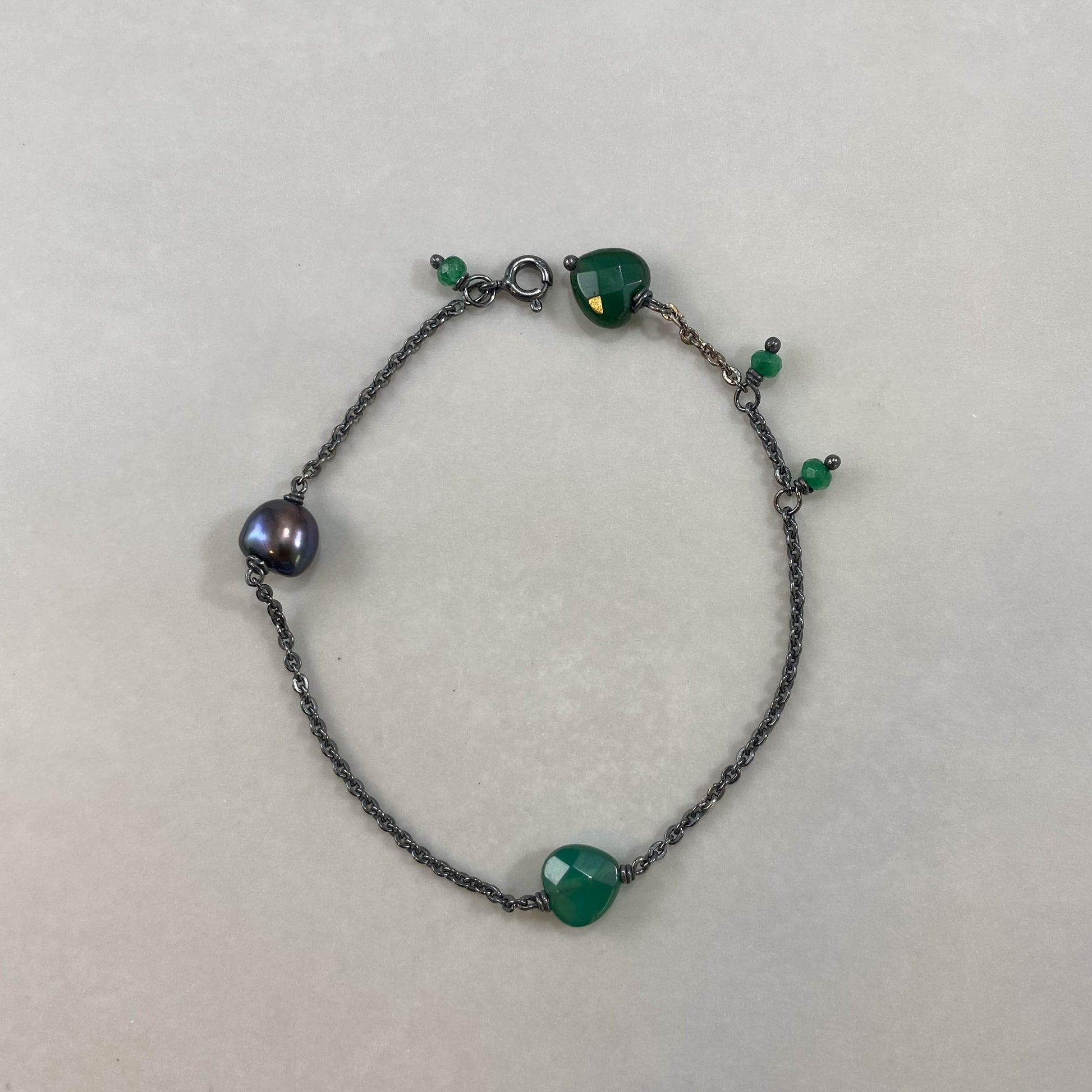 Pulseira corrente cartier redonda prata 925 oxidada (escura), com pingentes em pedras coração ágata verde e pérola negra. Comprimento: regulagem entre 15cm e 18cm. Para outras medidas entre em contato. Embalagem em envelope de tecido, com cartão postal Amor Maior. Esta é uma joia de prata 925 produzida com uma liga conhecida internacionalmente com STERLING SILVER – 925, o que significa que ela é constituída de 92,5% de prata pura, garantindo a qualidade do material utilizado. Por se tratar de pedras naturai