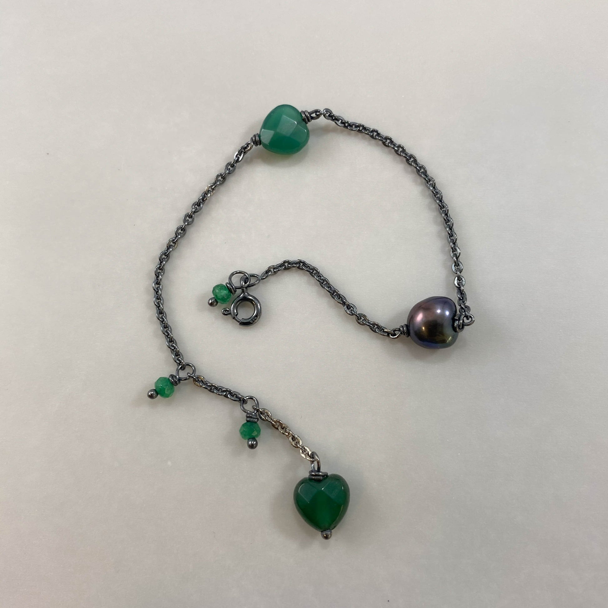 Pulseira corrente cartier redonda prata 925 oxidada (escura), com pingentes em pedras coração ágata verde e pérola negra. Comprimento: regulagem entre 15cm e 18cm. Para outras medidas entre em contato. Embalagem em envelope de tecido, com cartão postal Amor Maior. Esta é uma joia de prata 925 produzida com uma liga conhecida internacionalmente com STERLING SILVER – 925, o que significa que ela é constituída de 92,5% de prata pura, garantindo a qualidade do material utilizado. Por se tratar de pedras naturai