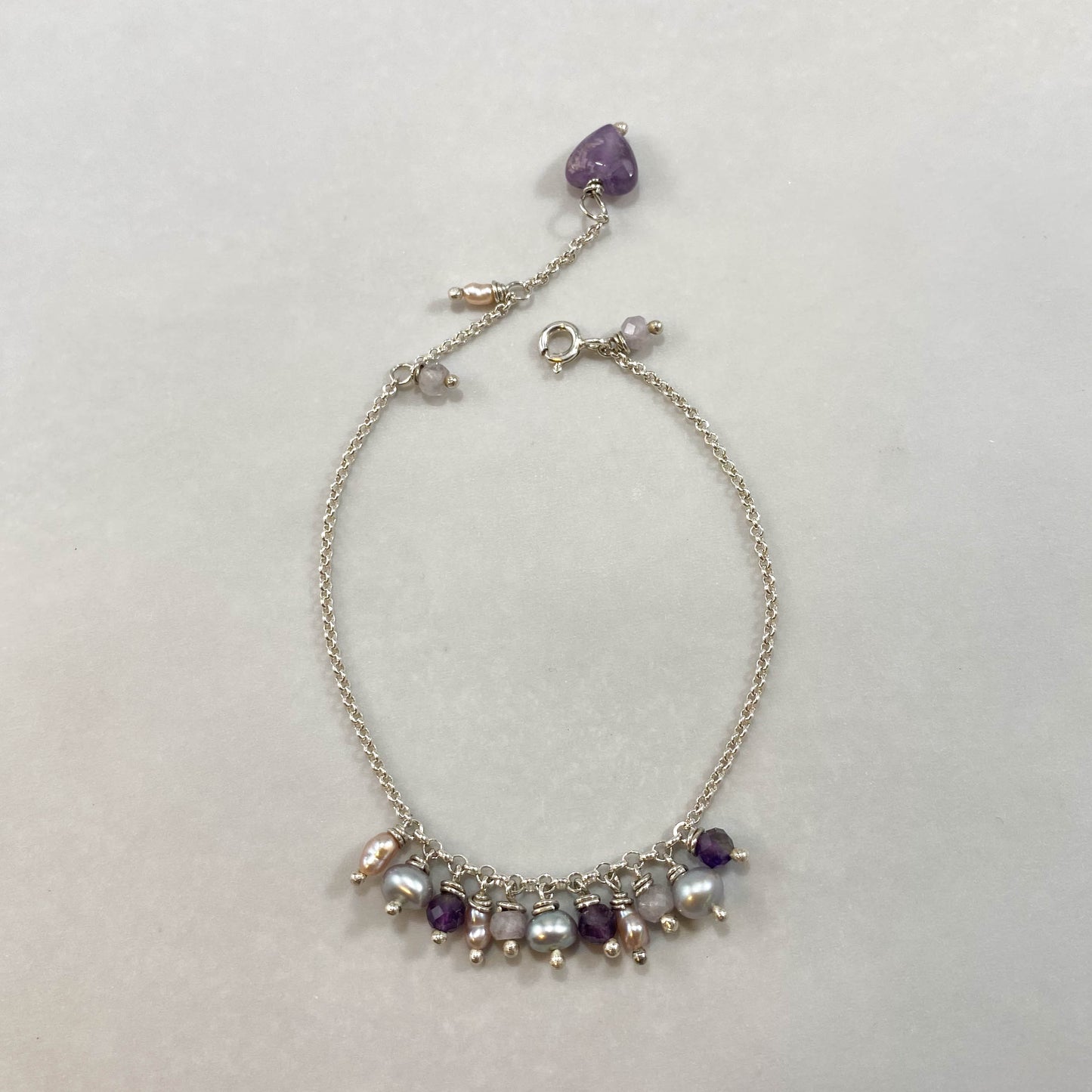 Pulseira corrente elo português em prata 925 polida (clara), com pedras ametista lavanda, pérolas e ametista. Comprimento: regulagem entre 15cm e 18cm. Para outras medidas entre em contato. Embalagem em envelope de tecido, com cartão postal Amor Maior. Esta é uma joia de prata 925 produzida com uma liga conhecida internacionalmente com STERLING SILVER – 925, o que significa que ela é constituída de 92,5% de prata pura, garantindo a qualidade do material utilizado. Por se tratar de pedras naturais, podem apr