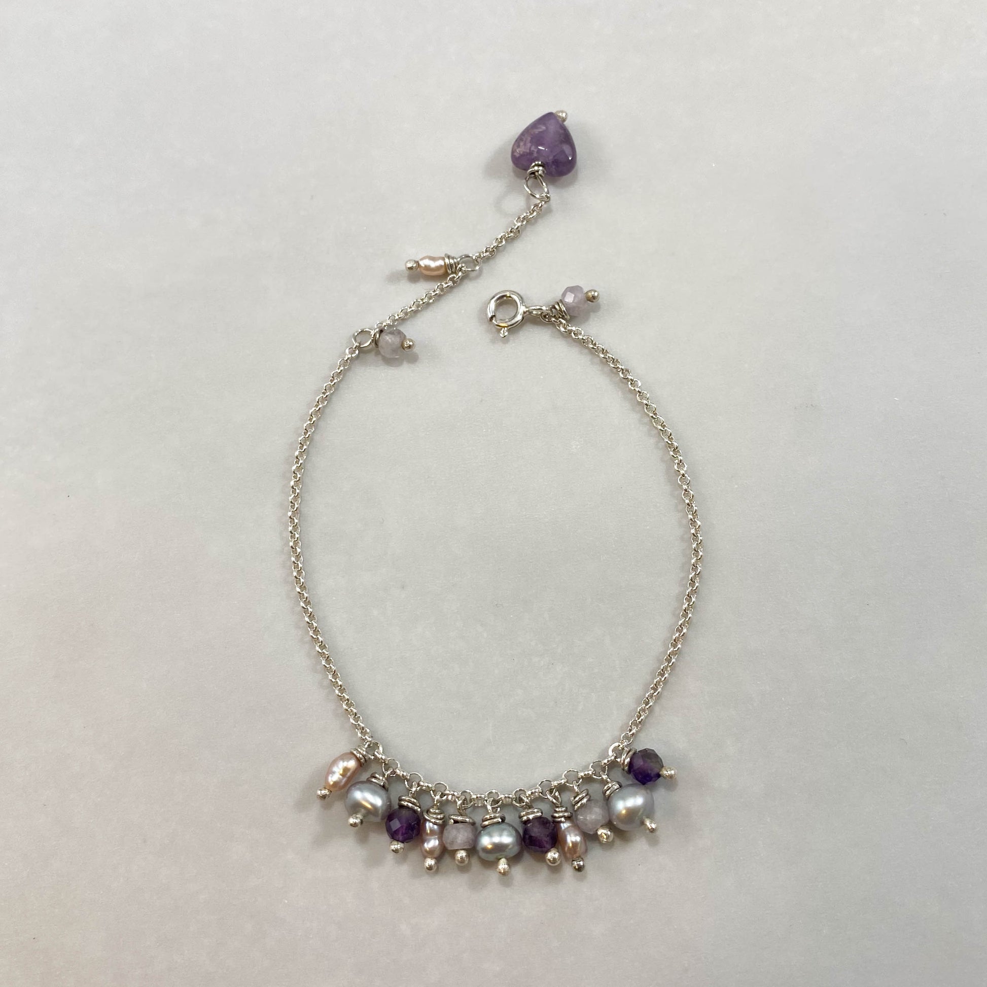 Pulseira corrente elo português em prata 925 polida (clara), com pedras ametista lavanda, pérolas e ametista. Comprimento: regulagem entre 15cm e 18cm. Para outras medidas entre em contato. Embalagem em envelope de tecido, com cartão postal Amor Maior. Esta é uma joia de prata 925 produzida com uma liga conhecida internacionalmente com STERLING SILVER – 925, o que significa que ela é constituída de 92,5% de prata pura, garantindo a qualidade do material utilizado. Por se tratar de pedras naturais, podem apr