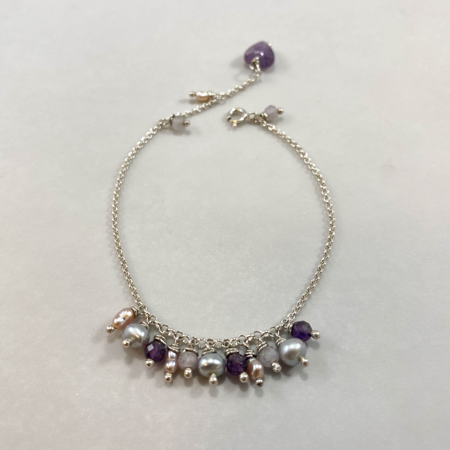 Pulseira corrente elo português em prata 925 polida (clara), com pedras ametista lavanda, pérolas e ametista. Comprimento: regulagem entre 15cm e 18cm. Para outras medidas entre em contato. Embalagem em envelope de tecido, com cartão postal Amor Maior. Esta é uma joia de prata 925 produzida com uma liga conhecida internacionalmente com STERLING SILVER – 925, o que significa que ela é constituída de 92,5% de prata pura, garantindo a qualidade do material utilizado. Por se tratar de pedras naturais, podem apr