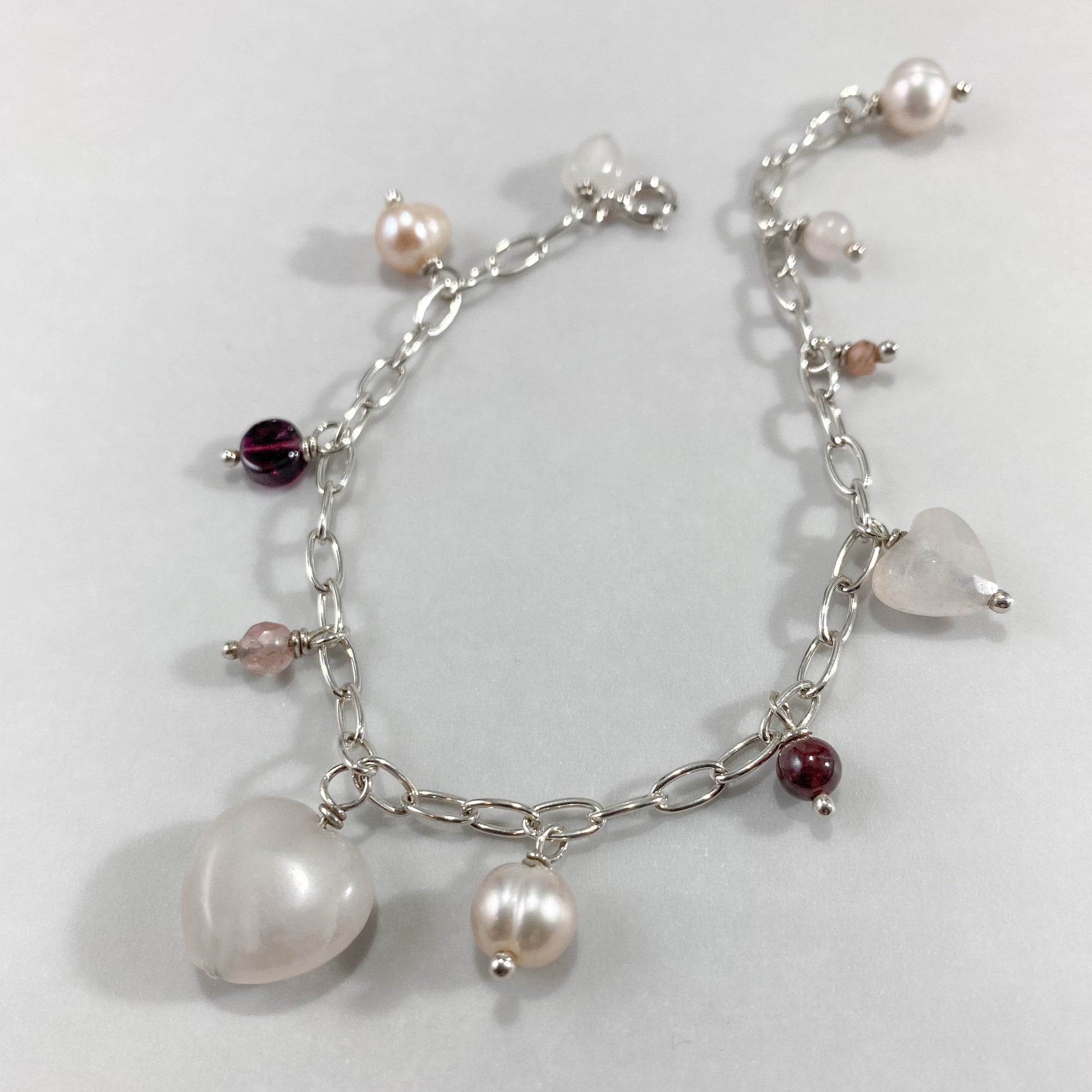 Pulseira corrente elos ovais prata 925 polida (clara), com pingentes em pedras quartzo rosa, pérola lilás, granada, quartzo cereja e rodocrosita. Comprimento: regulagem entre 15cm e 18cm. Para outras medidas entre em contato. Embalagem em envelope de tecido, com cartão postal Amor Maior. Esta é uma joia de prata 925 produzida com uma liga conhecida internacionalmente com STERLING SILVER – 925, o que significa que ela é constituída de 92,5% de prata pura, garantindo a qualidade do material utilizado. Por se 