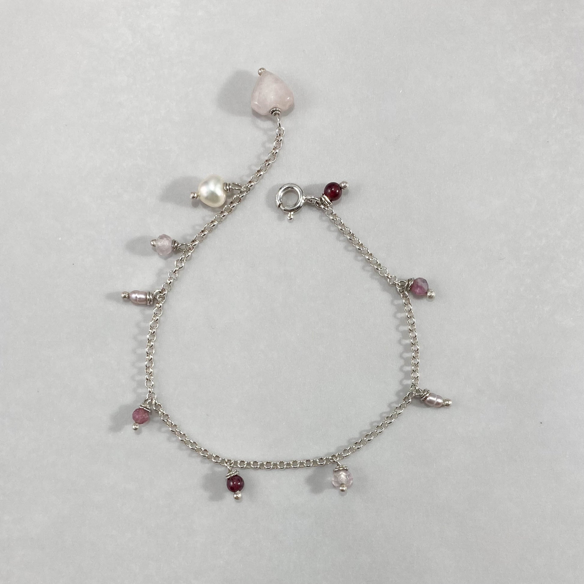 Pulseira corrente elo português aberto em prata 925 polida (clara), com pingentes em pedras quartzo rosa, pérola lilás, granada, quartzo cereja e rodocrosita. Comprimento: regulagem entre 15cm e 18cm. Para outras medidas entre em contato. Embalagem em envelope de tecido, com cartão postal Amor Maior. Esta é uma joia de prata 925 produzida com uma liga conhecida internacionalmente com STERLING SILVER – 925, o que significa que ela é constituída de 92,5% de prata pura, garantindo a qualidade do material utili