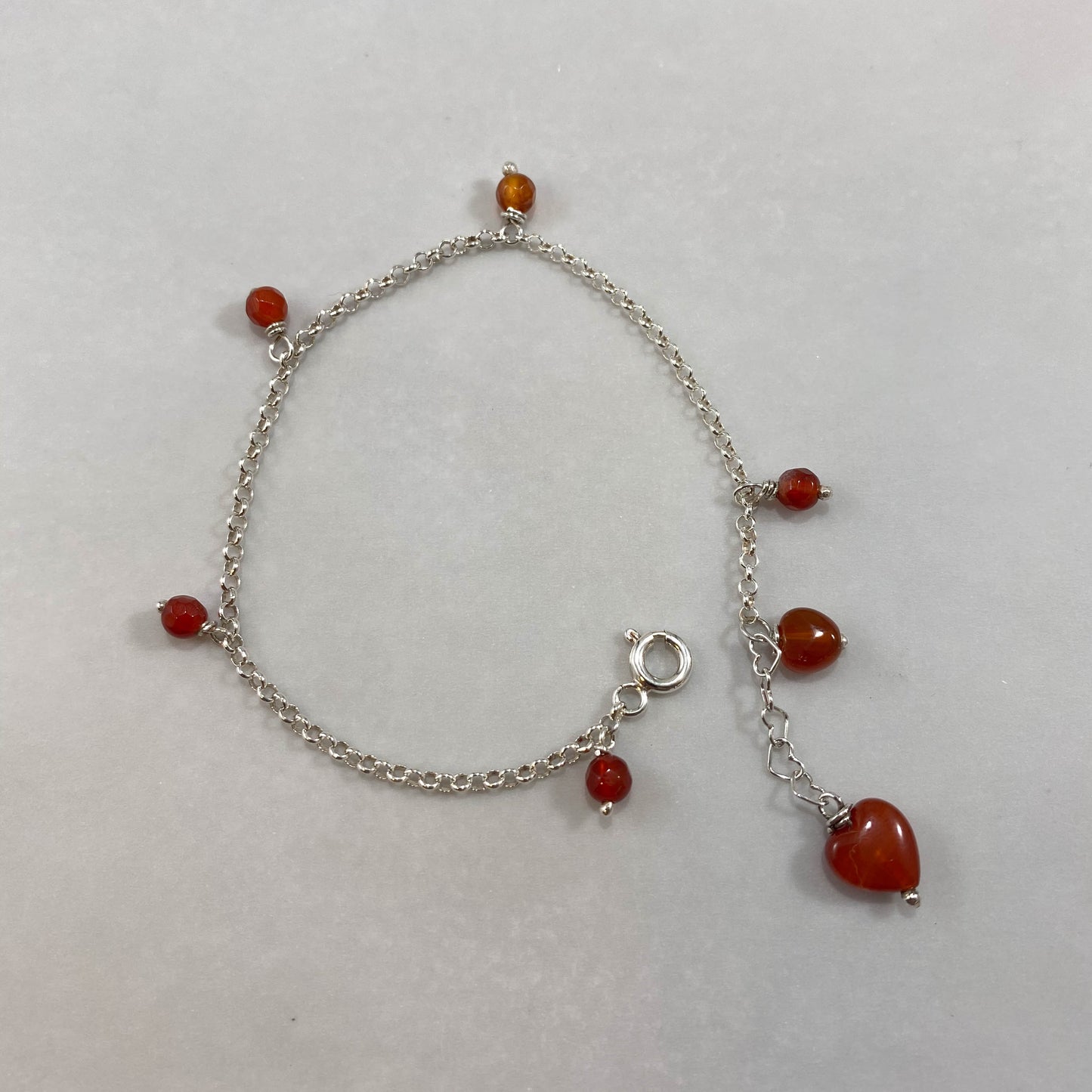 Pulseira corrente elo português prata 925 polida (clara), com pingentes em pedras ágata cornalina. Comprimento: regulagem entre 15cm e 18cm. Para outras medidas entre em contato. Embalagem em envelope de tecido, com cartão postal Amor Maior. Esta é uma joia de prata 925 produzida com uma liga conhecida internacionalmente com STERLING SILVER – 925, o que significa que ela é constituída de 92,5% de prata pura, garantindo a qualidade do material utilizado. Por se tratar de pedras naturais, podem apresentar var