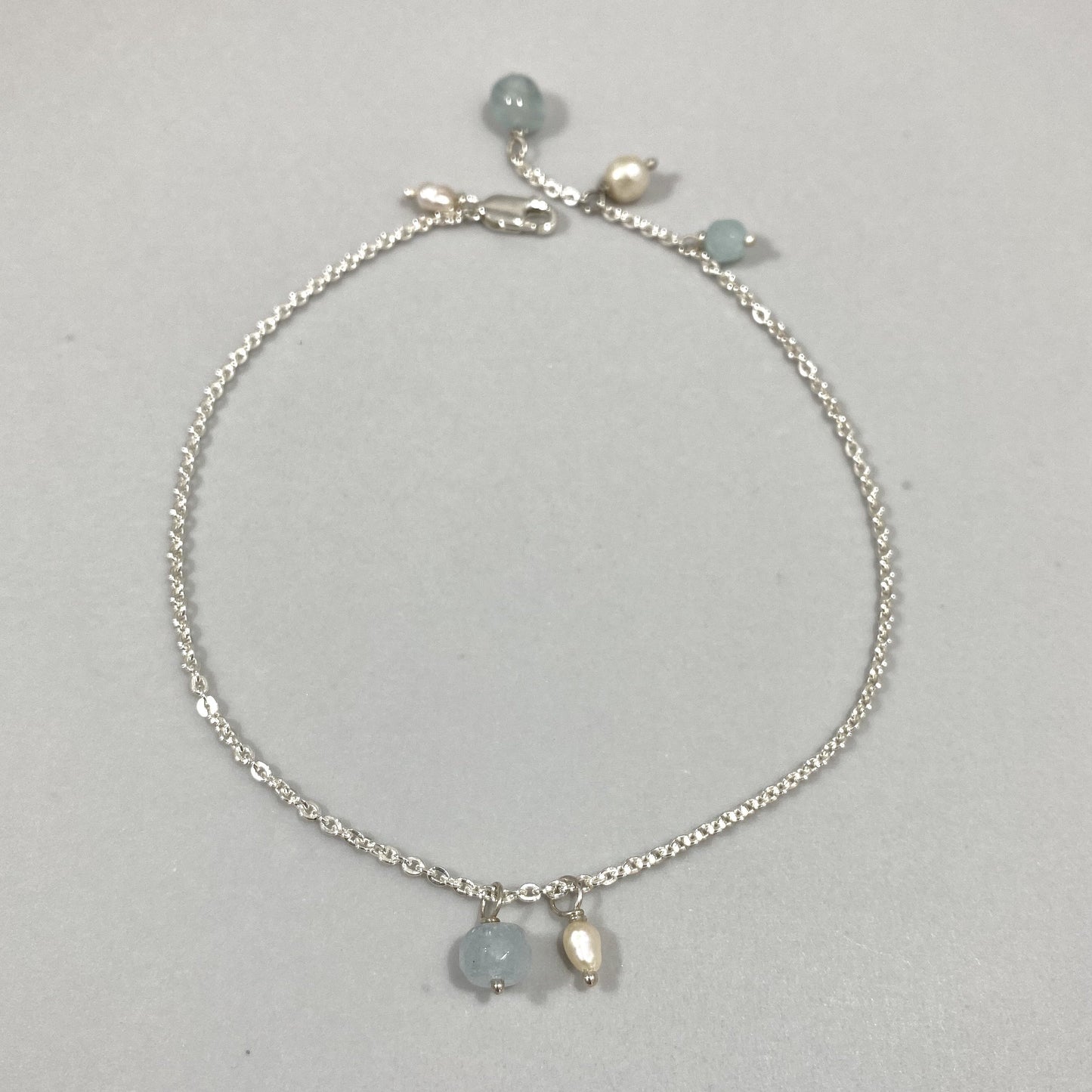 Tornozeleira corrente cartier em prata 925 polida (clara), com pedras água-marinha e pérolas. Comprimento: regulagem entre 23cm e 25,5cm. Para outras medidas entre em contato. Embalagem de algodão Santacosta. Esta é uma joia de prata 925 produzida com uma liga conhecida internacionalmente com STERLING SILVER – 925, o que significa que ela é constituída de 92,5% de prata pura, garantindo a qualidade do material utilizado. Por se tratar de pedras naturais, podem apresentar variações na coloração.